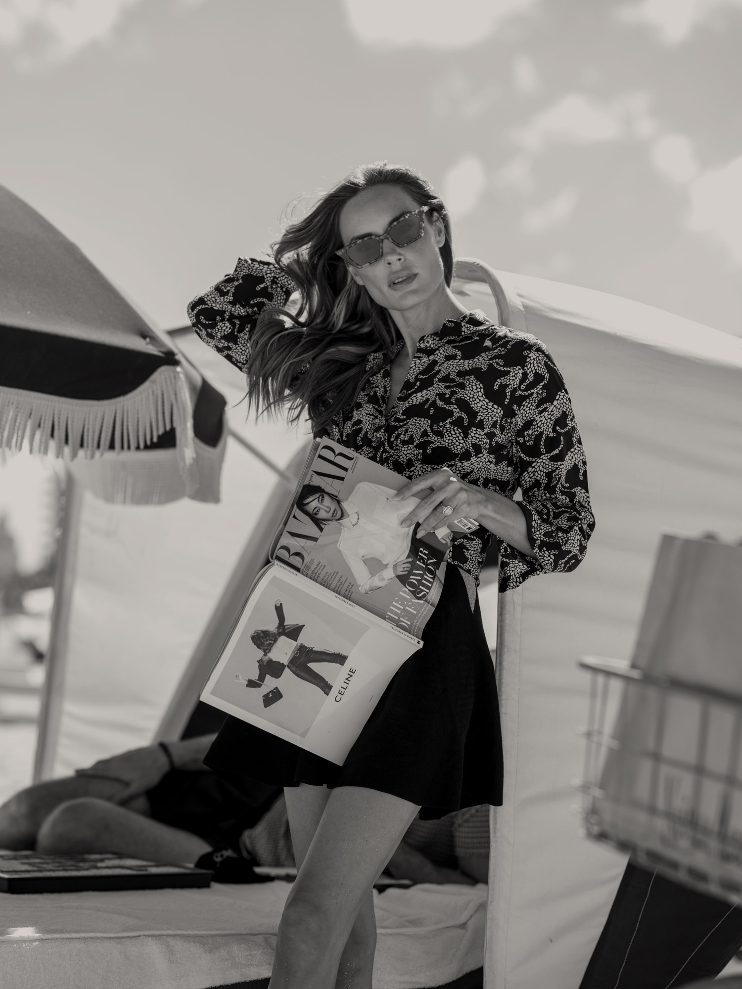 woman in sunglasses posing outdoors, holding a Bazaar magazine