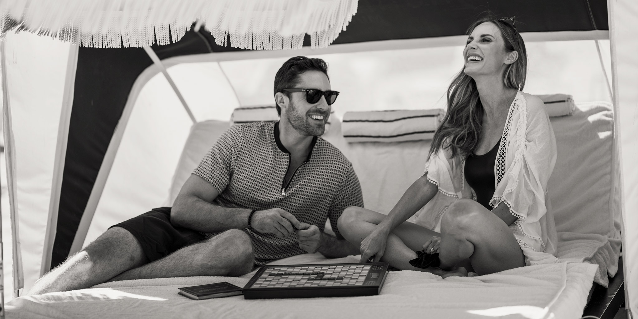 two people laughing while playing Scrabble in cabana