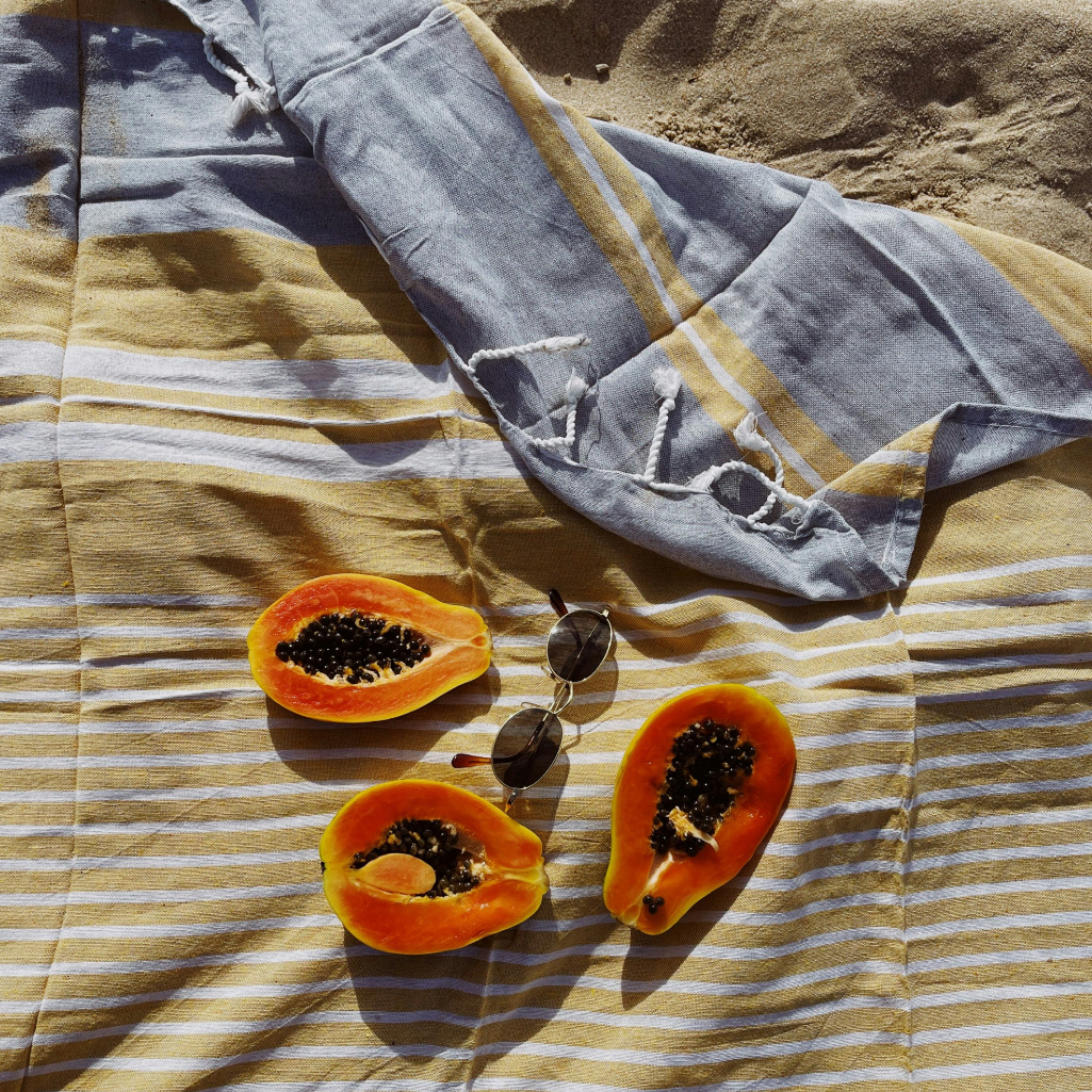 sliced papaya sitting alongside a pair of sunglasses on a beach towel