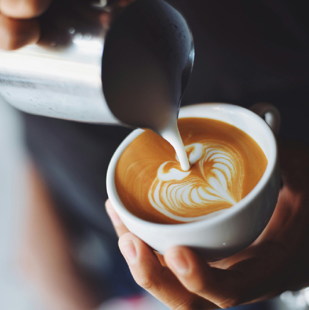 person pouring a cappuccino into a cup